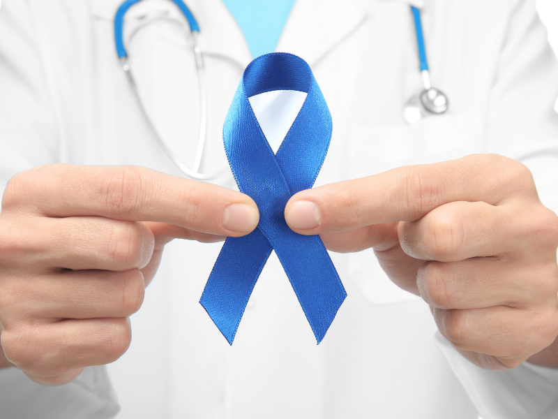 Doctor holding blue ribbon symbolizing cancer awareness and surgical oncology care at Vasavi Hospitals Bangalore.
